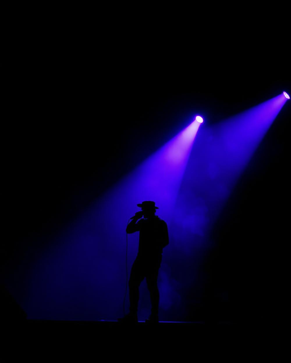 Silhouette of a performer under a single violet spotlight